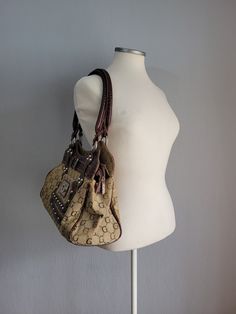 Make a statement with our Vintage Canvas and Leather Handbag in Brown and Gray by Gold Bags, a fusion of elegance and functionality. Crafted with meticulous attention to detail, this embellished zipped shoulder bag for women is adorned with crystals and rivets, adding a touch of glamour to your ensemble. The combination of brown leather and gray canvas lends a contemporary edge to its classic silhouette. Featuring a magnetic closure pocket on the front and a zipped pocket on the back, it offers Elegant Hobo Tote Bag, Shoulder Bag With Silver-tone Hardware For Fashion Accessory, Fashion Accessory Shoulder Bag With Silver-tone Hardware, Silver-tone Hardware Shoulder Bag, Elegant Pouch Shoulder Bag With Metal Hardware, Gold Bags, Gold Bag, Vintage Canvas, Classic Silhouette