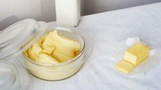 a bowl of butter next to a bottle of milk and some pieces of cheese on a table