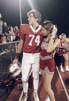 a man and woman in football uniforms walking on the sidelines with fans behind them