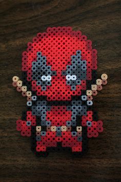 a red and black beaded deadpool brooch sitting on top of a wooden table