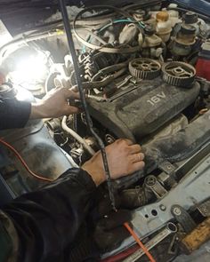 a man working on an engine in a car with the hood up and wires attached to it