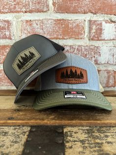 Evergreen tree line genuine leather patch hat. Many genuine leather patch and Richardson 112 hat color styles to choose from. Choose which patch color to put with each hat. American owned and operated with fast turnaround. Leather Hat Patch Designs, Trucker Style Baseball Cap With Patches For Outdoor, Outdoor Trucker Snapback Hat With Patches, Trucker Baseball Cap With Patches For Outdoor, Leather Patch Trucker Hat For Camping, Outdoor Trucker Hat With Patches And Curved Brim, Outdoor Trucker Hat With Leather Patch And Flat Bill, Trucker Hat With Leather Patch For Outdoor Activities, Trucker Style Snapback Hat With Leather Patch