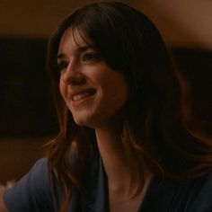 a woman with long hair smiling and looking to the side in a dark room while wearing a blue shirt