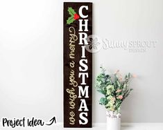 a wooden christmas sign next to a potted plant and vase with flowers in it