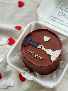 a chocolate cake in a plastic container with one year written on the side and hearts scattered around it