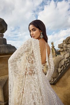 a woman in a white gown standing next to a stone wall and looking off into the distance