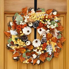 a wreath is hanging on the front door with autumn leaves and pumpkins around it