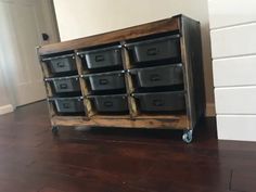 a wooden cart with black plastic containers on it's wheels in front of a white wall