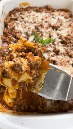 a spatula scooping some food out of a casserole dish with meat and cheese