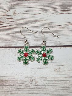 the green and red snowflake earrings are hanging from silver hooks on a white wooden surface