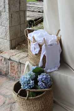 two wicker baskets with blue flowers and clothes hanging from them on a stone patio