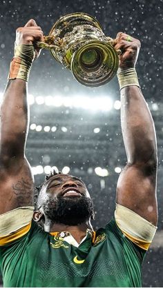 a man holding up a trophy above his head in the rain at a football game