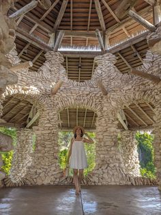 a woman standing in front of a stone building with arches and windows on the ceiling