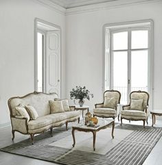 a living room filled with lots of furniture in front of two large windows and a rug on the floor