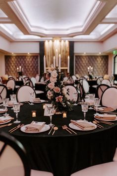 a black table topped with lots of white and pink flowers sitting next to tall candles