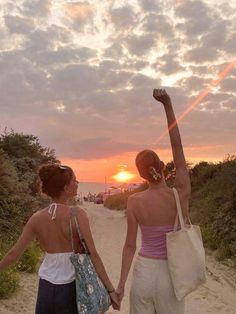 two women walking on the beach holding hands and raising their arms in the air as the sun sets