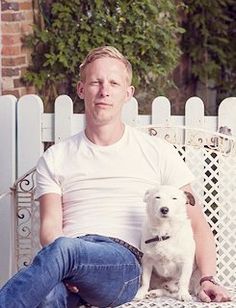 a man sits on a bench with his dog in front of him and looks at the camera