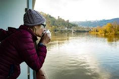 a woman drinking from a cup while standing next to a river