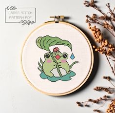 a cross stitch pattern with a green frog holding a flower in it's mouth