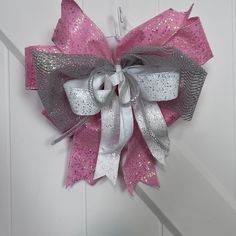 a pink and silver bow hanging on the side of a white door with glitters