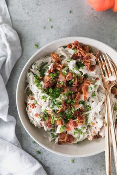 a white bowl filled with mashed potatoes and bacon on top of a gray table