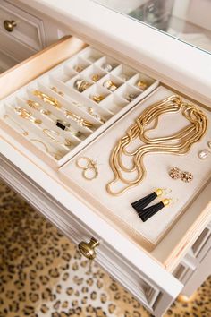 an organized drawer with gold jewelry and black tassels on it's drawers