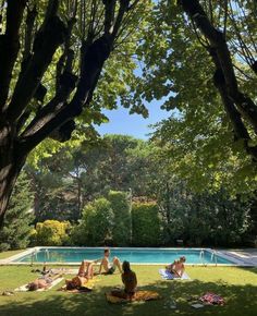 people are sitting on the grass near a swimming pool and some trees in front of them