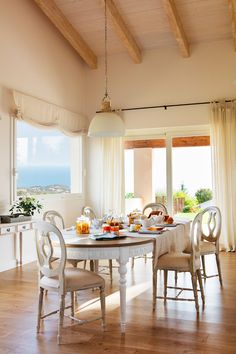 a dining room table and chairs in front of an open window with the ocean outside