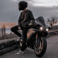 a man sitting on top of a black motorcycle next to a stone wall and wearing a helmet