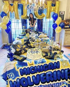 a table topped with cake and balloons in front of a party sign that says michigan wolverines