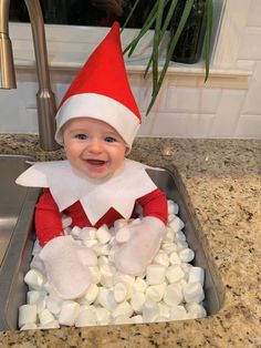 a baby in a sink with marshmallows on it's feet and wearing a santa hat