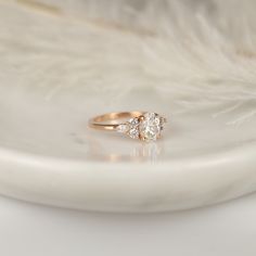 a diamond ring sitting on top of a white plate with feathers in the back ground