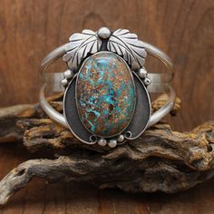 Large sterling silver and turquoise cuff bracelet. A plate soldered on the back is stamped "WP." The artist's hallmark is unknown. The bracelet face is 2 1/4" wide. The stone is 40mm long. The stone is a pretty turquoise with lots of brown matrix. Two handmade leaves and some silver balls add to the design. The cuff has two 5mm rounded wire shanks that connect at the ends. "Sterling" is stamped on one shank. The bracelet is in good condition. Thank you for shopping in our store. Please let us kn Artisan Sterling Silver Cuff Bracelet With Patina, Vintage Silver Chrysocolla Jewelry, Rustic Silver Jewelry With Patina, Vintage Sterling Silver Cuff Bracelet With Patina, Turquoise Bracelet Cuff, Jewelry Antique, Turquoise Cuff, Inspired Jewelry, American Jewelry