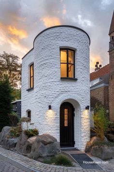 a white brick house with a black door and windows on the outside, surrounded by rocks