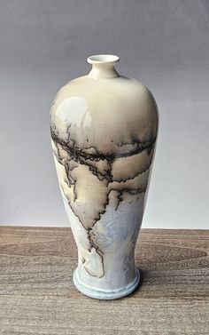 a white and black vase sitting on top of a wooden table next to a wall