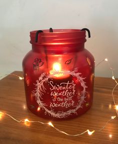 a red glass jar sitting on top of a wooden table next to a string of lights