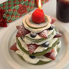 a stack of pancakes covered in fruit and topped with a lit candle next to a cup of coffee