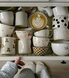 a drawer full of cups and saucers with someone's feet on the shelf