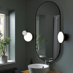 a bathroom sink sitting under a round mirror next to a window with potted plants