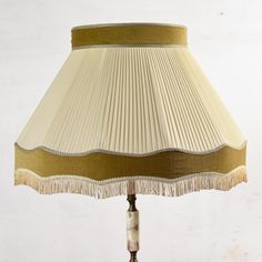 a lamp that is sitting on top of a wooden base with fringed lampshade