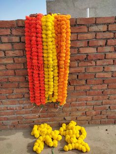 some yellow and orange pom poms hanging from a brick wall next to bricks