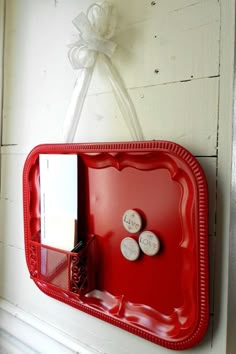 a red tray with two clocks on it and a note holder attached to the wall