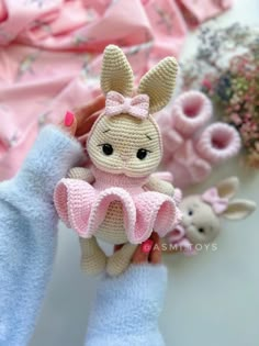 a crocheted bunny doll is held up by someone's hand with pink gloves