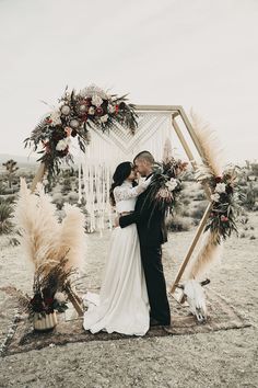 a newly married couple kissing in front of an arch decorated with flowers and pamodia