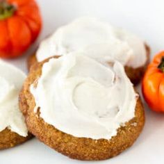 three cookies with frosting and mini pumpkins in the background on a white surface