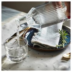 a person pouring water into a glass on top of a plate with napkins and glasses