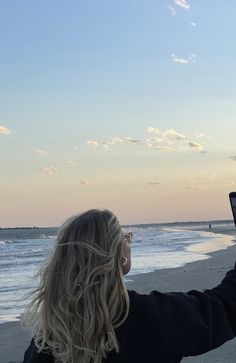 a woman standing on top of a sandy beach next to the ocean holding a cell phone