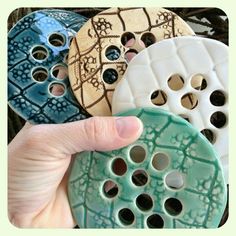 a hand is holding four different colored ceramic buttons with holes in the middle and bottom