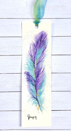 a watercolor painting of a purple and blue feather on a white wooden background with a green ribbon