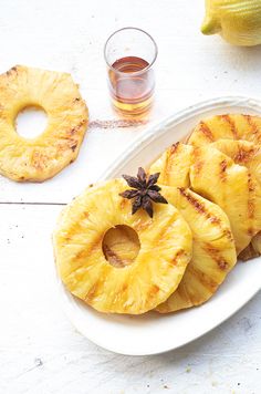 grilled pineapple slices on a white plate next to a shot glass and fruit